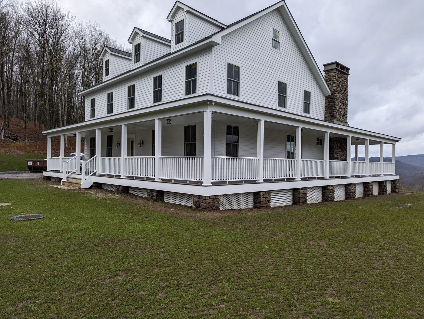The full wraparound porch, dormers and stone chimney